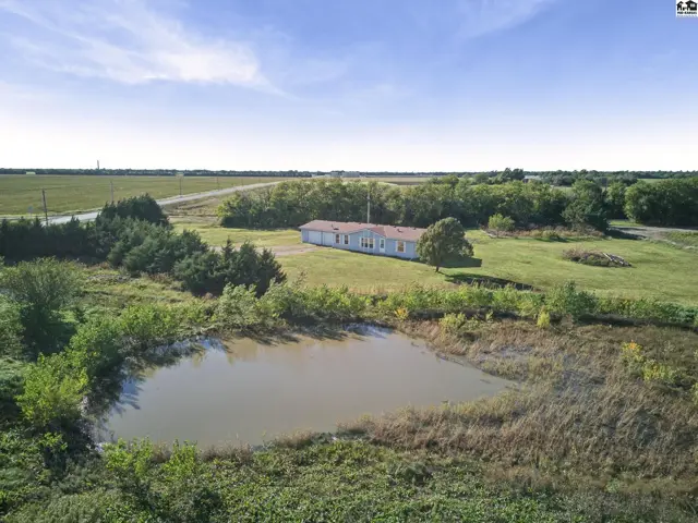 A white ranch-style house with a dark roof sits on a grassy lot with a pond.