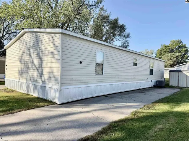 This manufactured home features beige siding, white skirting, and a concrete driveway.