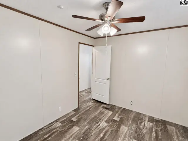 This room features wood-look flooring, white paneled walls, and a ceiling fan.