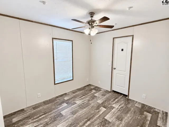 This room features wood-look flooring, a ceiling fan, and a white door.