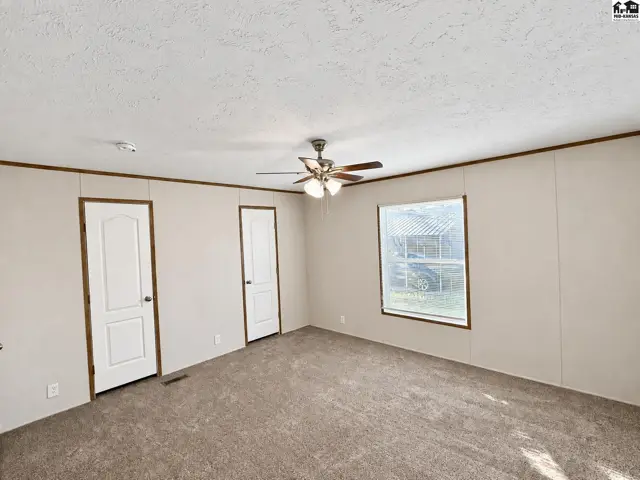 Carpeted room with two doors, a ceiling fan, and a large window.