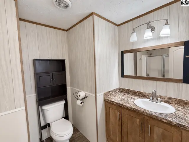 This bathroom features a vanity with a granite-look countertop, a toilet, and a shower.