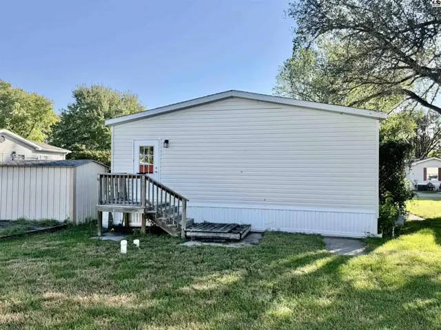 This manufactured home features vinyl siding, a wooden deck, and a storage shed.