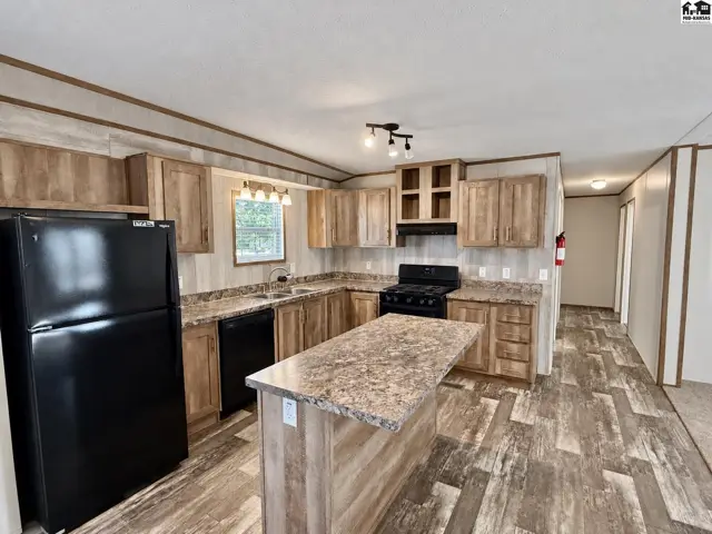 This kitchen features light wood cabinetry, a central island, and a black gas range.