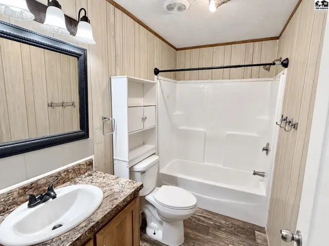 This bathroom features a vanity with a granite-look countertop, a white toilet, and a white tub-shower combination.