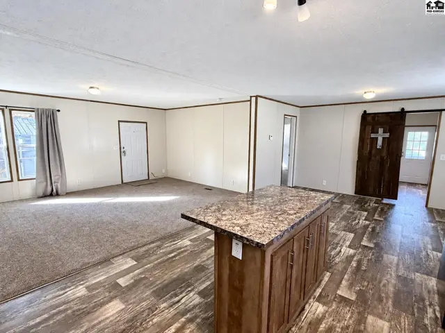 Spacious living area with carpet, wood-look flooring, and a granite-topped island.