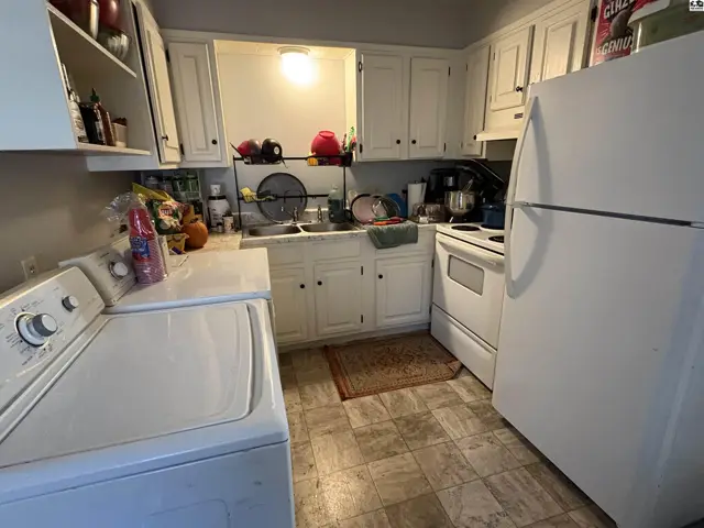 White cabinets, a white refrigerator, stove, and washer are in this kitchen with a patterned floor.