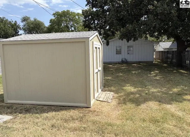 A light-colored storage shed with a double door sits on a grassy yard.