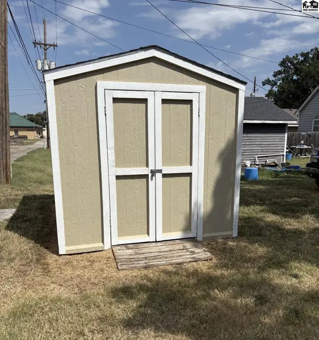 Tan shed with white trim and double doors sits on a grassy yard.