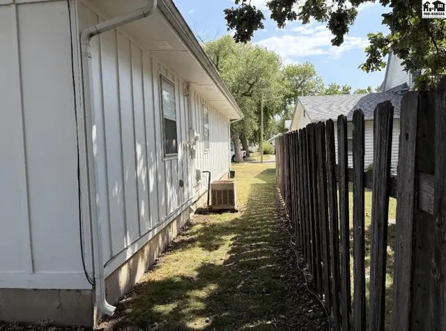 White siding and a wooden fence line a grassy yard with an air conditioning unit.