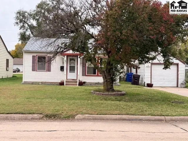 White vinyl-sided home with red trim, a detached garage, and mature landscaping.