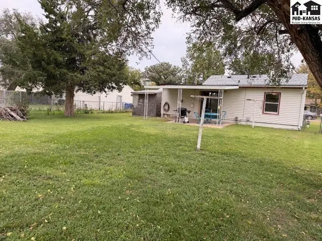 A white house with a covered patio and a large, grassy yard.