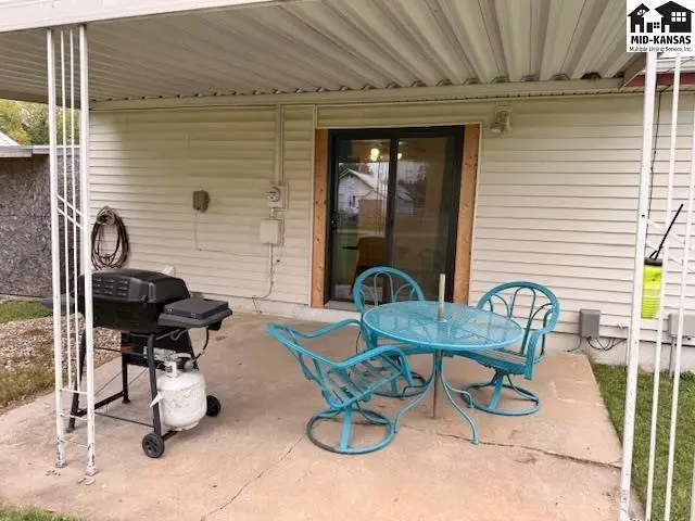 Covered patio with a table, chairs, and grill overlooks a concrete slab.
