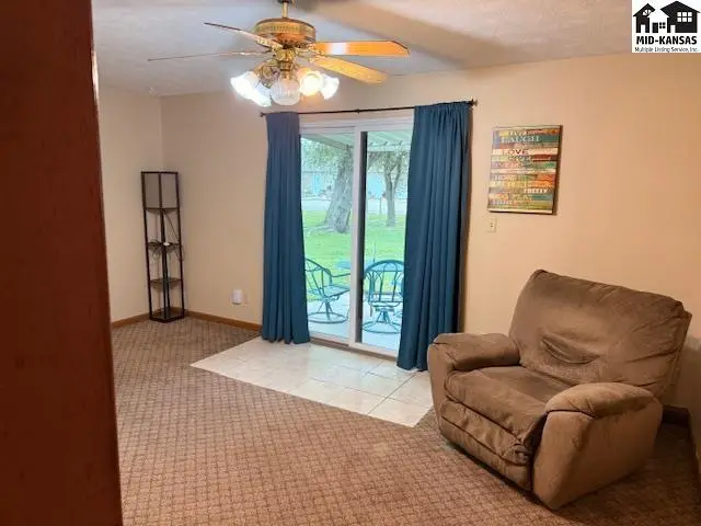 Carpeted living area with sliding glass doors, ceiling fan, and a recliner.