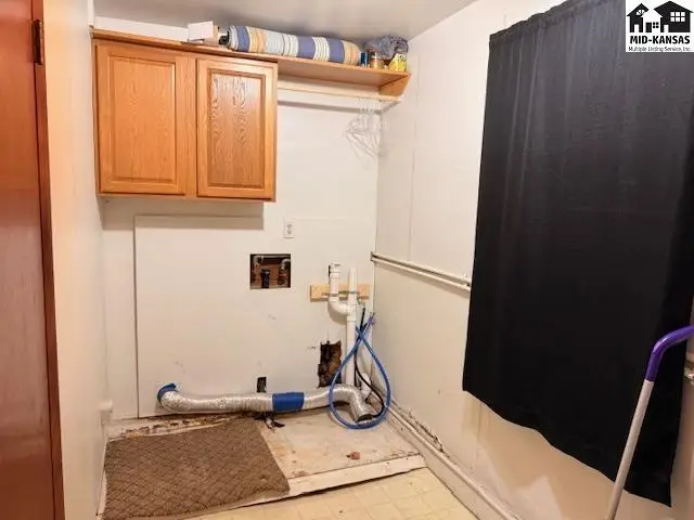 This laundry room features wood cabinetry, vinyl flooring, and plumbing hookups.