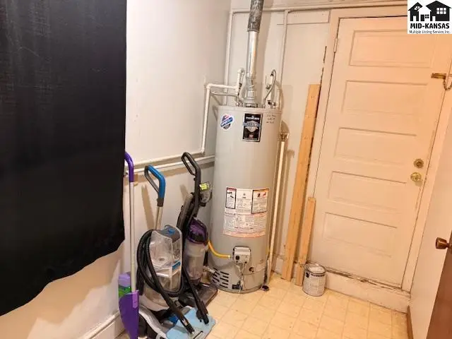A water heater, vacuum cleaner, and mop are in a room with a white door.