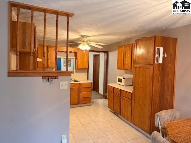 Kitchen features wood cabinetry, tiled flooring, and a ceiling fan.