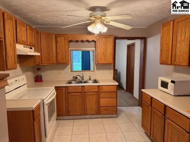 Kitchen features wood cabinetry, a double sink, and a ceiling fan.