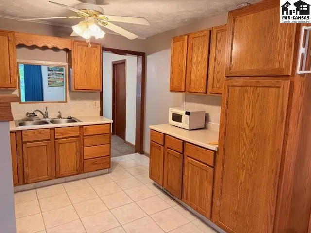 Kitchen features wood cabinetry, a double sink, and a ceiling fan.