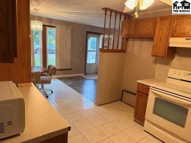 Kitchen with white appliances and wood cabinets opens to a dining area and living room.