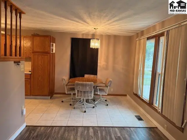 Dining area with wood table, chairs, tiled floor, and large windows.