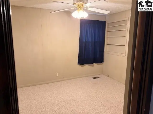 Carpeted room with a ceiling fan, window, and built-in shelving.