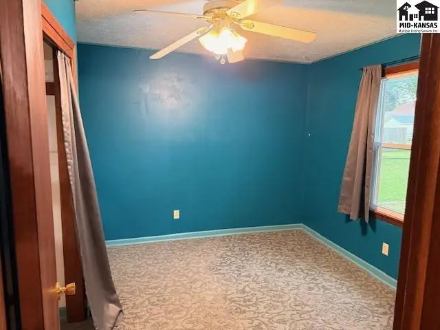 This room features teal walls, a patterned carpet, and a ceiling fan.