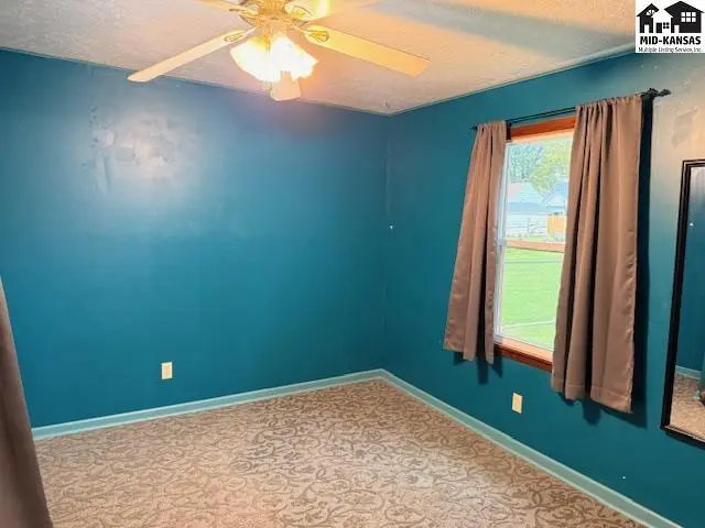 This room features teal walls, a patterned carpet, and a ceiling fan.
