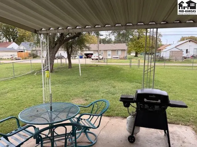 Covered patio with seating and grill overlooks a fenced yard.