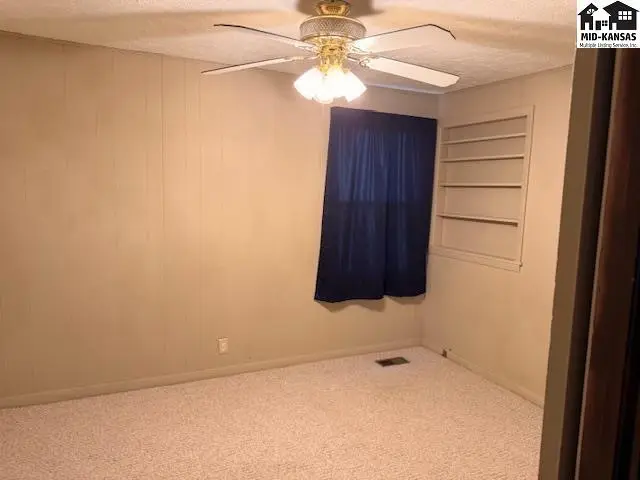 Carpeted room features a ceiling fan, window with blue curtains, and built-in shelving.