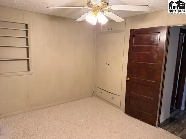 Carpeted room with a ceiling fan, built-in storage, and a wooden door.