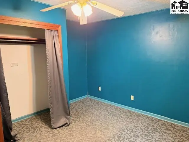 This room features teal walls, patterned carpet, and a ceiling fan.